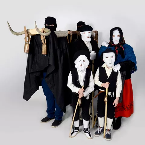 Adultos y niños con máscaras blancas y cencerros.