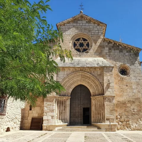 Fachada románica de piedra con gran portada arqueada y rosetón circular.