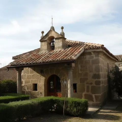 Pequeña ermita de piedra con tejado a dos aguas y jardín delantero.