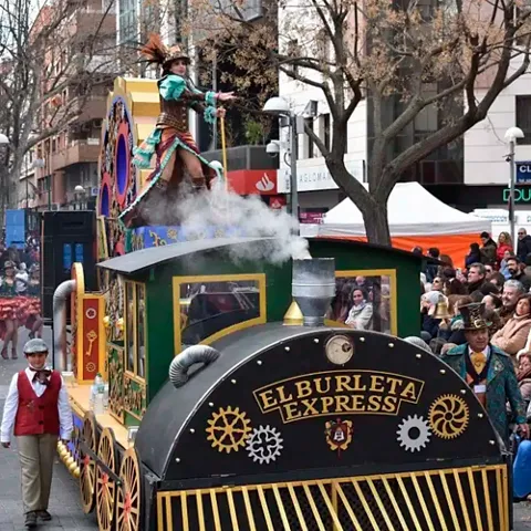 Carroza con locomotora decorativa y personajes disfrazados en un desfile multitudinario.