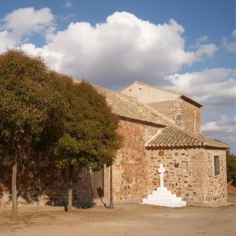 Iglesia de Caracuel de Calatrava construida en piedra, con cruz blanca y pequeña plaza en primer plano.
