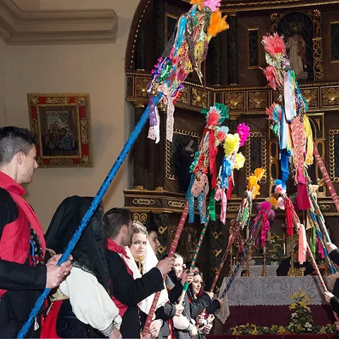 Personas con trajes tradicionales levantando varas decoradas dentro de una iglesia.