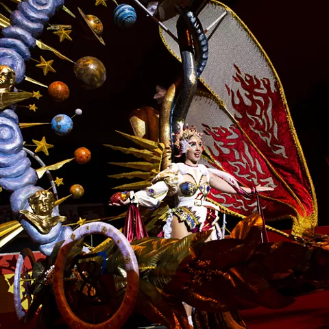 Carroza iluminada con figura femenina y decoración de planetas y estrellas en desfile nocturno.