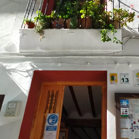 Fachada blanca con balcón con plantas y entrada a edificio cultural.