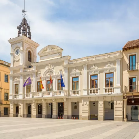 Edificio institucional con reloj y balcones con banderas.