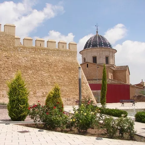 Muralla de piedra con almenas junto a cúpula de edificio histórico.