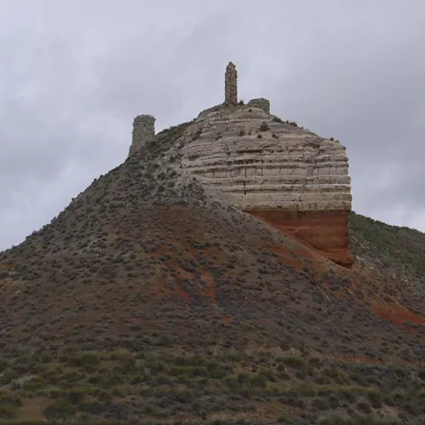 Cerro escarpado con restos de torres y murallas de piedra en la cima.