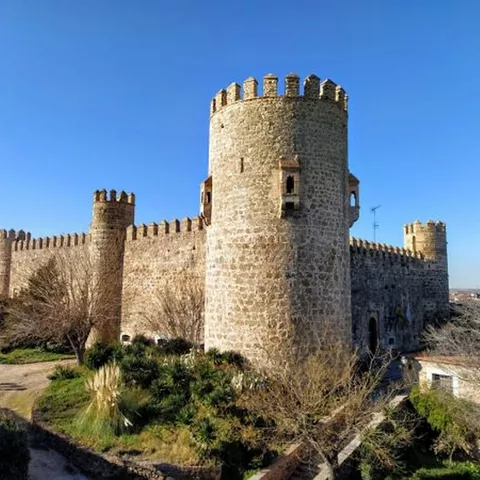 Vista lateral de fortaleza amurallada con torre del homenaje y jardín exterior.