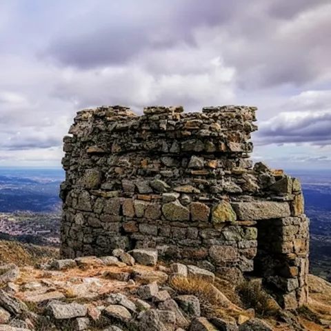 Torre de piedra en ruinas con vistas a un valle bajo cielo nublado.