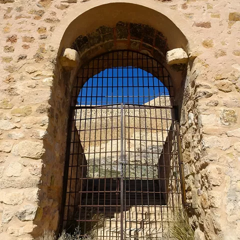 Puerta en arco con reja metálica en muro de piedra.