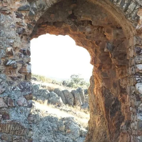 Arco de acceso en muro de piedra con paisaje al fondo