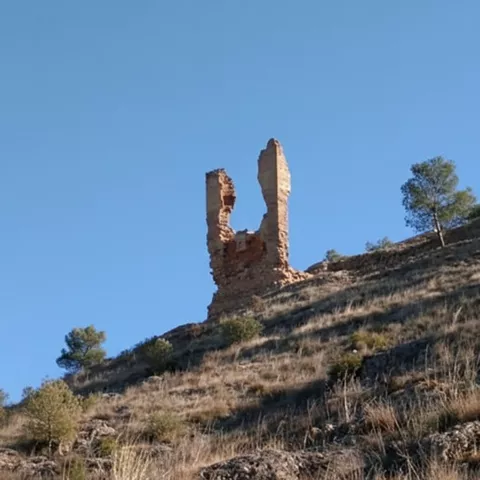 Restos de muralla en lo alto de una colina seca, bajo un cielo azul despejado.
