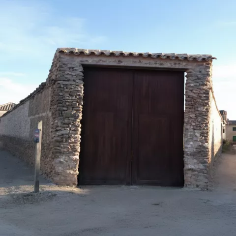 Gran portón de madera en un edificio de piedra, en un cruce de calles del pueblo.