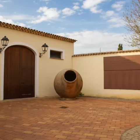 Patio con gran puerta de madera y una tinaja monumental junto a un panel mural.