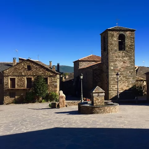 Plaza con casas de piedra y torre campanario.
