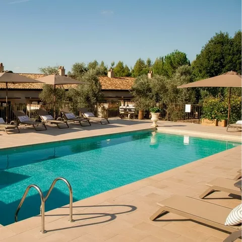 Piscina al aire libre con tumbonas y sombrillas junto a jardines.