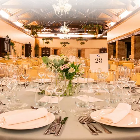 Salón de eventos con mesas redondas, centros florales y copas