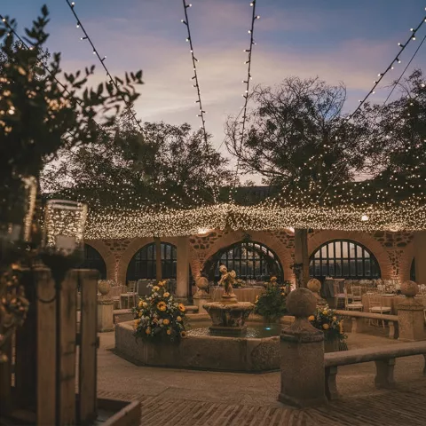 Patio decorado con fuente y guirnaldas de luces al anochecer.