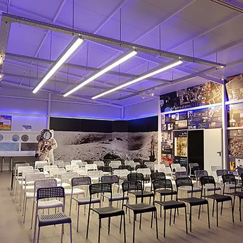 Sala expositiva con sillas en filas, mural lunar y figura de astronauta al fondo.