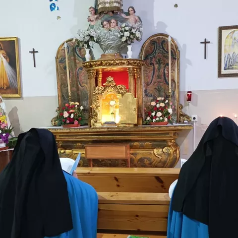Religiosas rezando en bancos de madera ante un altar, con un perro tumbado en el suelo.