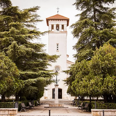 Edificio religioso blanco entre árboles y bancos de un parque