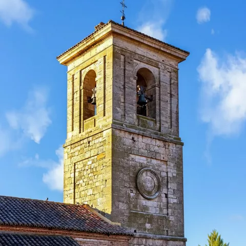 Torre campanario de iglesia sobre tejados tradicionales.