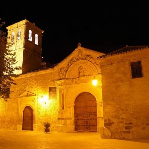 Iglesia iluminada de noche con portada monumental y torre campanario de piedra.