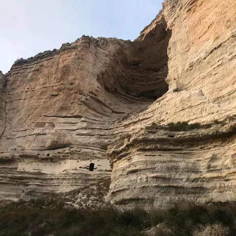 Pared rocosa estratificada con cavidad natural en lo alto del acantilado.
