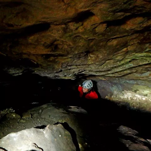 Espeleólogo avanzando por un paso bajo y estrecho entre rocas.