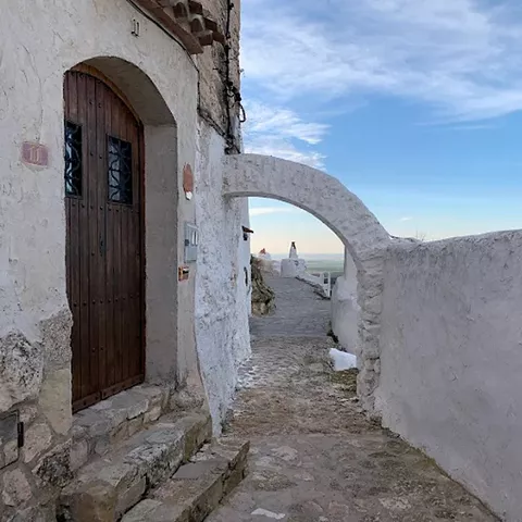 Calle estrecha entre casas cueva con arco de piedra y suelo empedrado.