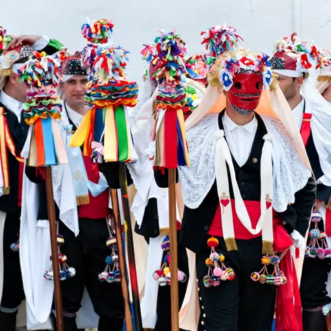 Grupo de personas enmascaradas con trajes tradicionales y bastones adornados.