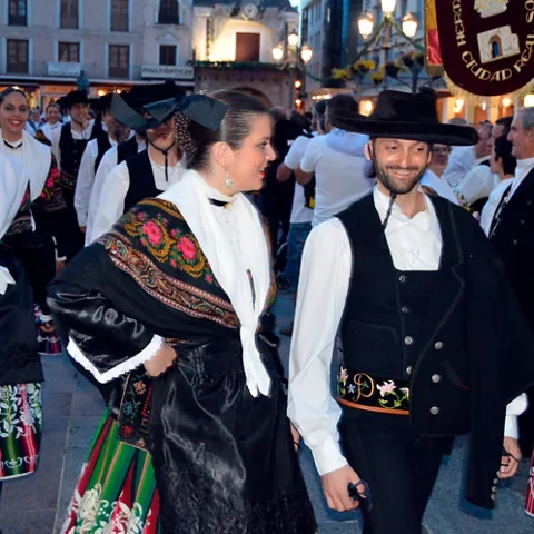 Desfile popular al atardecer con personas vestidas con trajes tradicionales y ramos de flores.