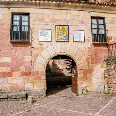 Fachada de piedra con arco de entrada y azulejo decorativo.