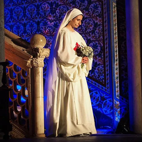 Actriz con hábito blanco y ramo de flores.