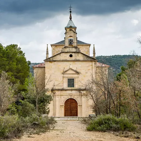 Fachada de templo de piedra entre árboles y camino rural.
