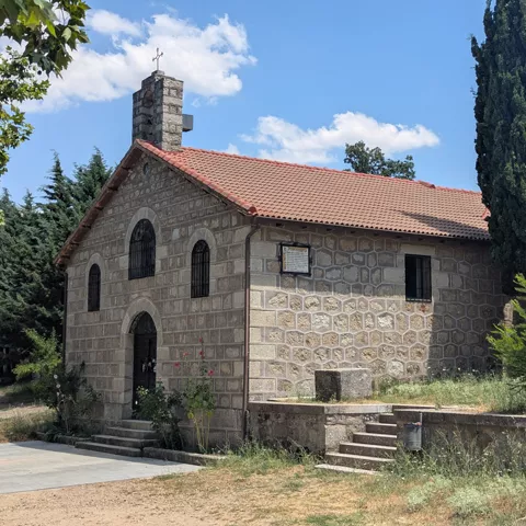 Camino nevado junto a una ermita de piedra y árboles alineados.