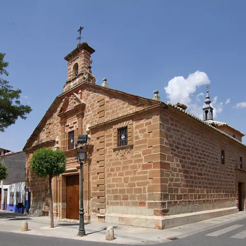 Ermita de piedra en esquina urbana y cielo azul.