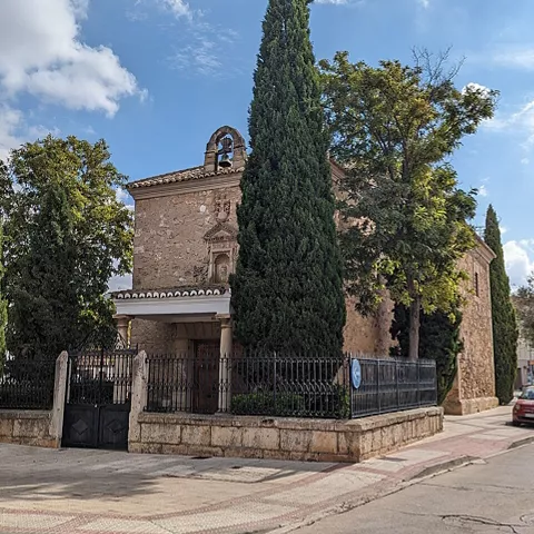 Ermita rodeada de cipreses en entorno urbano tranquilo.