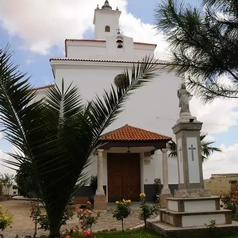Ermita blanca rodeada de jardín con palmeras y cruz de piedra