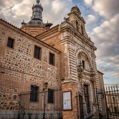 Iglesia histórica con portada monumental, muros de mampostería y cielo cubierto de nubes.