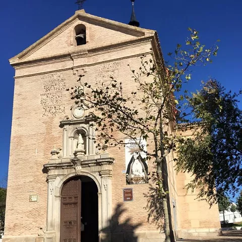 Entrada de iglesia con fachada de ladrillo y árbol en primer plano.