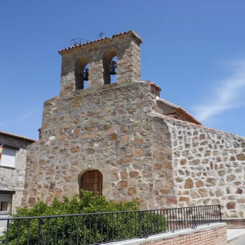 Construcción de piedra con espadaña y campanas en calle estrecha.
