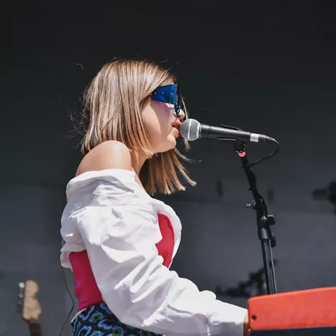 Cantante tocando teclado y cantando al micrófono en un escenario.