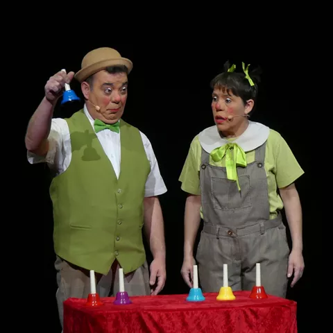 Dos intérpretes caracterizados realizando juego escénico con campanas de colores.