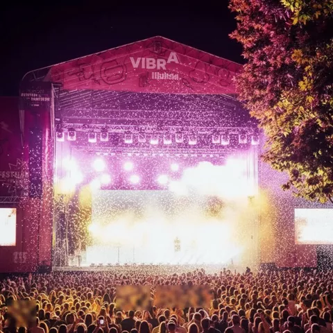 Escenario iluminado con confeti cayendo sobre público en concierto nocturno.