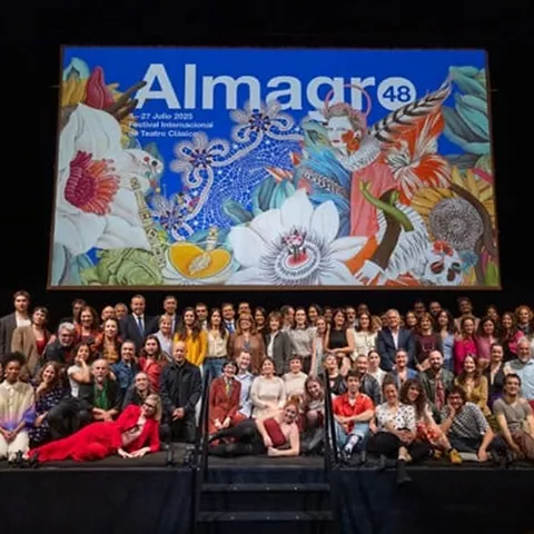 Escenario teatral con gran cartel ilustrado y grupo numeroso de personas posando tras una función.