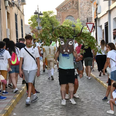 Figura enmascarada con ramas caminando por una calle concurrida