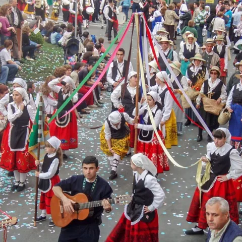 Desfile popular con músicos y personas vestidas con trajes tradicionales por una calle del pueblo.