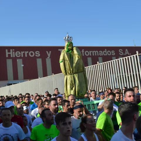 Multitud acompañando una imagen religiosa elevada durante una procesión urbana.