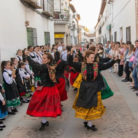 Baile tradicional en una calle, con dos bailarinas en primer plano y vecinos observando desde los laterales.